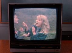 an old tv sitting on top of a wooden table next to a couple of people