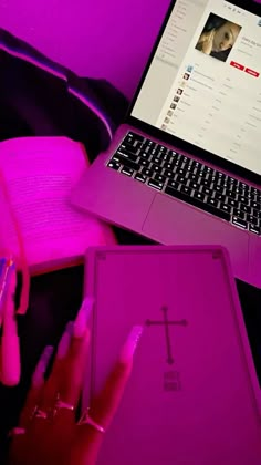 a laptop computer sitting on top of a desk next to a pink book and pen