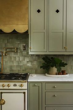 a white stove top oven sitting next to a green cabinet in a kitchen with gold accents