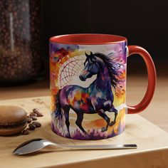 a colorful coffee mug sitting on top of a wooden table next to a spoon and fork