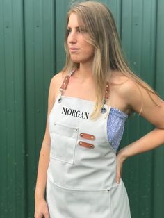 a woman wearing an apron with the word morgan on it, standing in front of a green wall