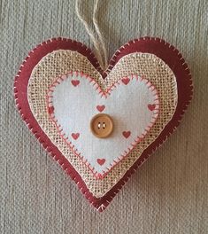 a heart shaped ornament with a button on it's side hanging from a string