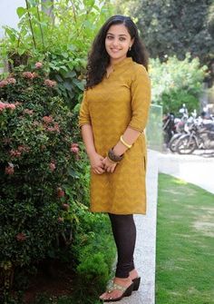 a woman standing in front of a bush with her hands on her hips and smiling