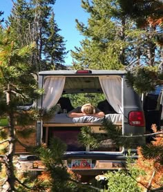 two people sleeping in the back of a pick up truck with trees around them and a tent on top