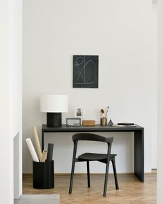 a black desk with two chairs and a lamp on it in front of a white wall