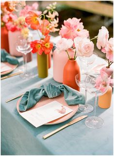 the table is set with pink and orange flowers in vases, napkins, and wine glasses