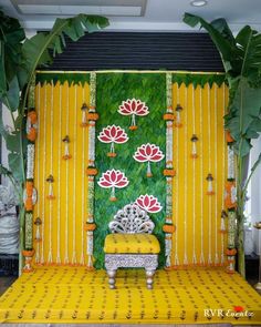 a yellow and white stage set up with flowers on the wall, green foliage in the background