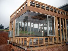 a house being built with wooden framing and glass windows on the front porch, overlooking an open field