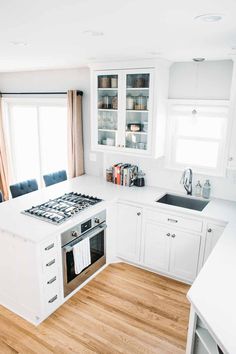 a kitchen with white cabinets and wood flooring is pictured in this image, there are two windows above the stove