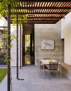 an outdoor dining area with table and chairs under a pergolated roof on the side of a house