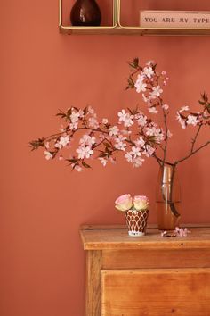 a vase filled with pink flowers sitting on top of a wooden table next to a wall