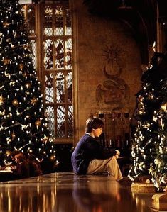 a woman sitting on the floor in front of a christmas tree and looking at her cell phone