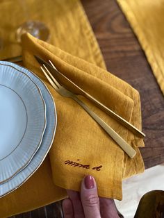 a person holding a fork and knife on top of a yellow napkin with gold trim