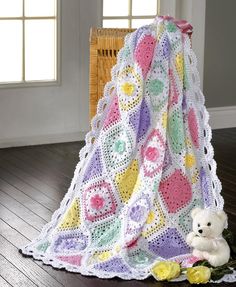 a white teddy bear sitting under a crocheted blanket on top of a wooden floor