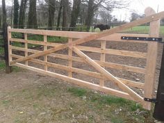 a wooden gate in the middle of a field with a horse standing behind it and trees