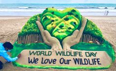 a man kneeling down in front of a sign on the beach that says, world wildlife day we love our wildlife