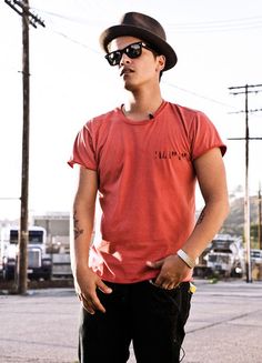 a young man wearing sunglasses and a hat standing on the street with his hands in his pockets