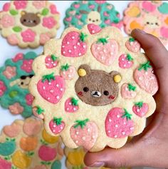 a hand holding up a decorated cookie in the shape of a bear and strawberrys