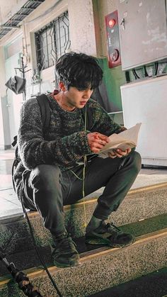 a young man sitting on the steps reading a paper while holding a microphone in his hand