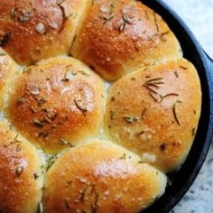 a cast iron skillet filled with rolls covered in cheese and rosemary sprinkled on top