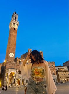 a woman is standing in front of a clock tower with her hand on her head