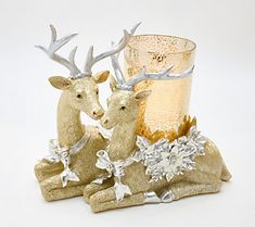 two deer figurines sitting next to each other near a glass vase and candle holder