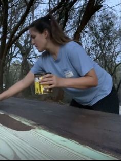 a woman holding a can of paint on the side of a road with trees in the background