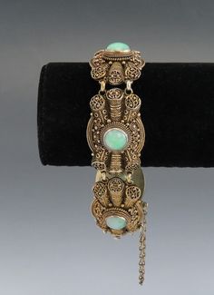 Presented is a stunning antique Chinese vermeil (gilt silver) and jade bracelet, dating to the late 1800s or early 1900s. The bracelet consists of five very ornate filigree links, each bezel set with a round cabochon of beautiful light green jade. The jade is a very appealing color, with natural mottling and variations but overall very well matched. The filigree is exceptionally intricate and finely done by hand, some of the highest quality you'll find. The bracelet closes with a tab insert styl Ornate Yellow Gold Bracelet Jewelry, Collectible Intricate Design Jewelry Bracelet, Traditional Oval Bracelets For Formal Occasions, Victorian Ceremonial Carved Jewelry, Antique Oval Hallmarked Bracelet, Formal Cabochon Bracelet Jewelry, Traditional Jade Jewelry For Weddings, Collectible Hallmarked Bracelet Jewelry, Collectible Hallmarked Bracelet