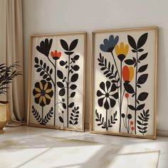 two framed art pieces with flowers and leaves on them in front of a white wall