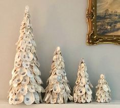 three ceramic christmas trees sitting on top of a shelf next to a painting and framed picture