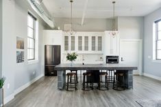 a large kitchen with white cabinets and black counter tops, along with two stools at the center island