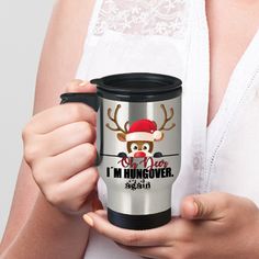 a woman holding a stainless steel travel mug with reindeer on the front and i'm hungover printed on it