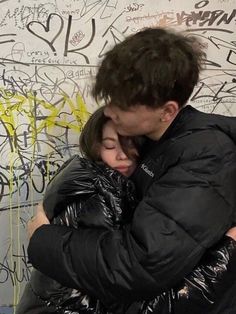 a man and woman hugging in front of graffiti covered wall