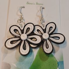 a pair of white and black flower shaped earrings on a card with a green background