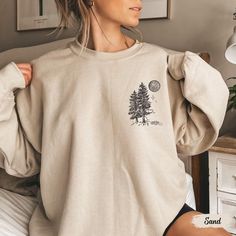 This sweatshirt, featuring a pocket design with pine trees and a moon, is a must-have for wilderness lovers and granola girls alike. Whether you're hiking, camping, or simply embracing your love for nature, this crewneck is the perfect blend of cozy and adventurous! Prefer this design on a T-Shirt? Visit this link: https://bohemianbloomdesigns.etsy.com/listing/1785034623/wilderness-shirt-pine-tree-shirt Prefer this design on a Hoodie? Visit this link: https://bohemianbloomdesigns.etsy.com/listin Long Sleeve T-shirt For Fall Adventure, Oversized Long Sleeve Tops For Outdoor, Outdoor Cotton Sweatshirt With Pockets, Cotton Sweatshirt With Pockets For Outdoor Activities, Comfortable Winter Tops With Pockets, Relaxed Fit Long Sleeve Tops For Outdoor, Comfortable Long Sleeve Sweatshirt For Outdoor Activities, Oversized Graphic Print Tops For Outdoor Activities, Relaxed Fit Long Sleeve Tops For Adventure