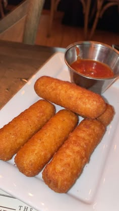 some fried food on a white plate with dipping sauce in a small metal bowl next to it