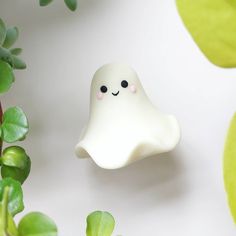 there is a small white ghost with eyes on it's head next to some plants