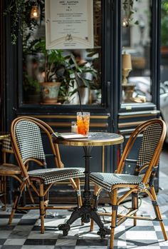 two chairs and a table in front of a storefront with an orange drink on it