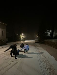 two people are playing in the snow with their skateboards at night time and one person is falling off his board