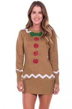 a woman wearing a brown sweater dress with red and green buttons on the chest, standing in front of a white background