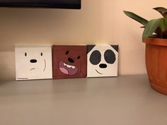 three paintings of panda, panda and panda bear faces are on the table next to a potted plant