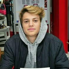 a young man sitting at a table in front of a laptop computer and wearing a hoodie