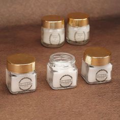 four small jars with gold lids sitting on top of a brown table next to each other