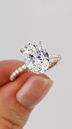 a person holding an oval diamond ring in their left hand, with the center stone surrounded by small diamonds