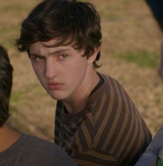 a close up of a person wearing a striped shirt and looking at another person in the background