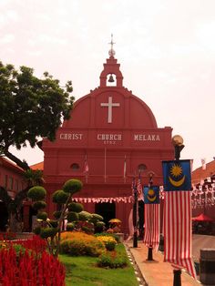 a red church with american flags in front of it and flowers on the ground around it