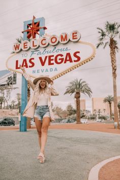 a woman walking in front of the welcome to las vegas sign with her hat on