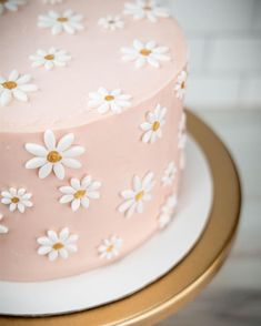 a pink cake with white daisies on it sitting on a gold plated stand