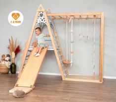 a baby sitting on top of a slide next to a wooden frame in a room