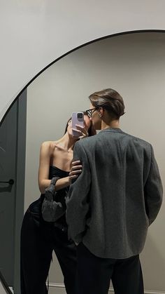 a woman taking a selfie in front of a mirror with a man standing next to her